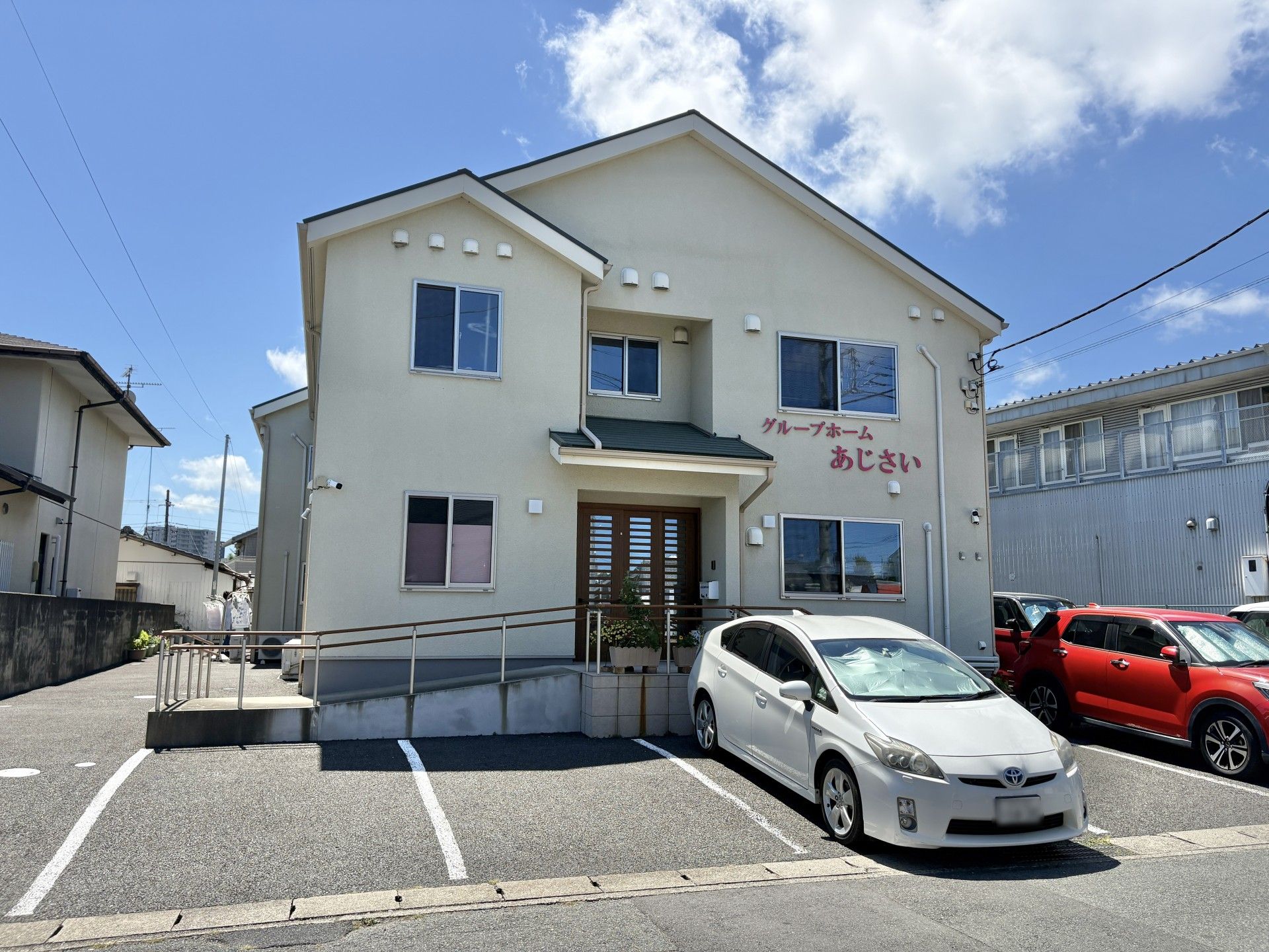 ピンクのエプロンを付けた若い女性スタッフとカーディガンを着た車いすの高齢女性が笑顔で話している。