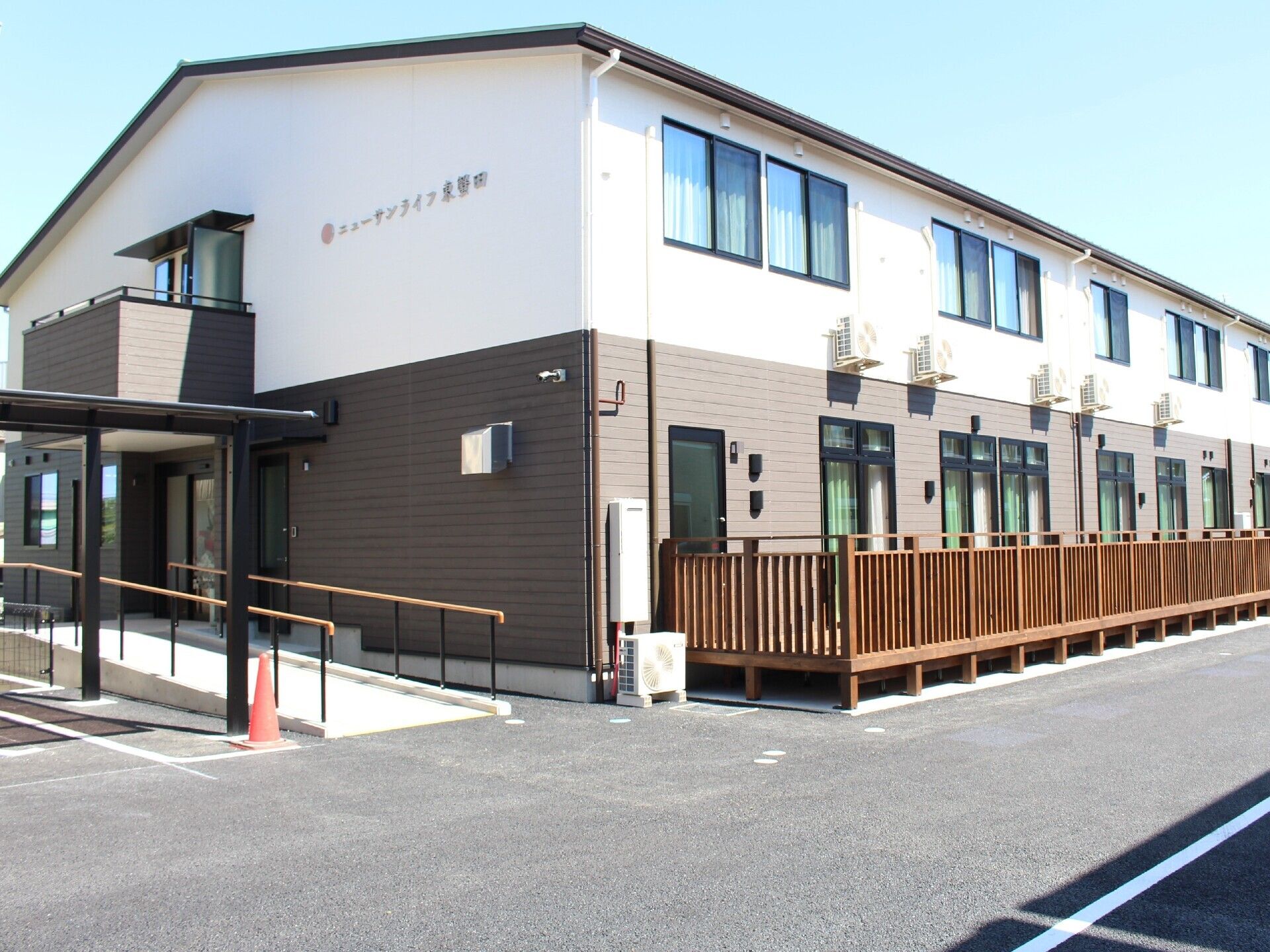2階建ての建物。1階部分はダークグレー、2階部分は白で、花や草木が植えられたスペースや広い駐車場もある。