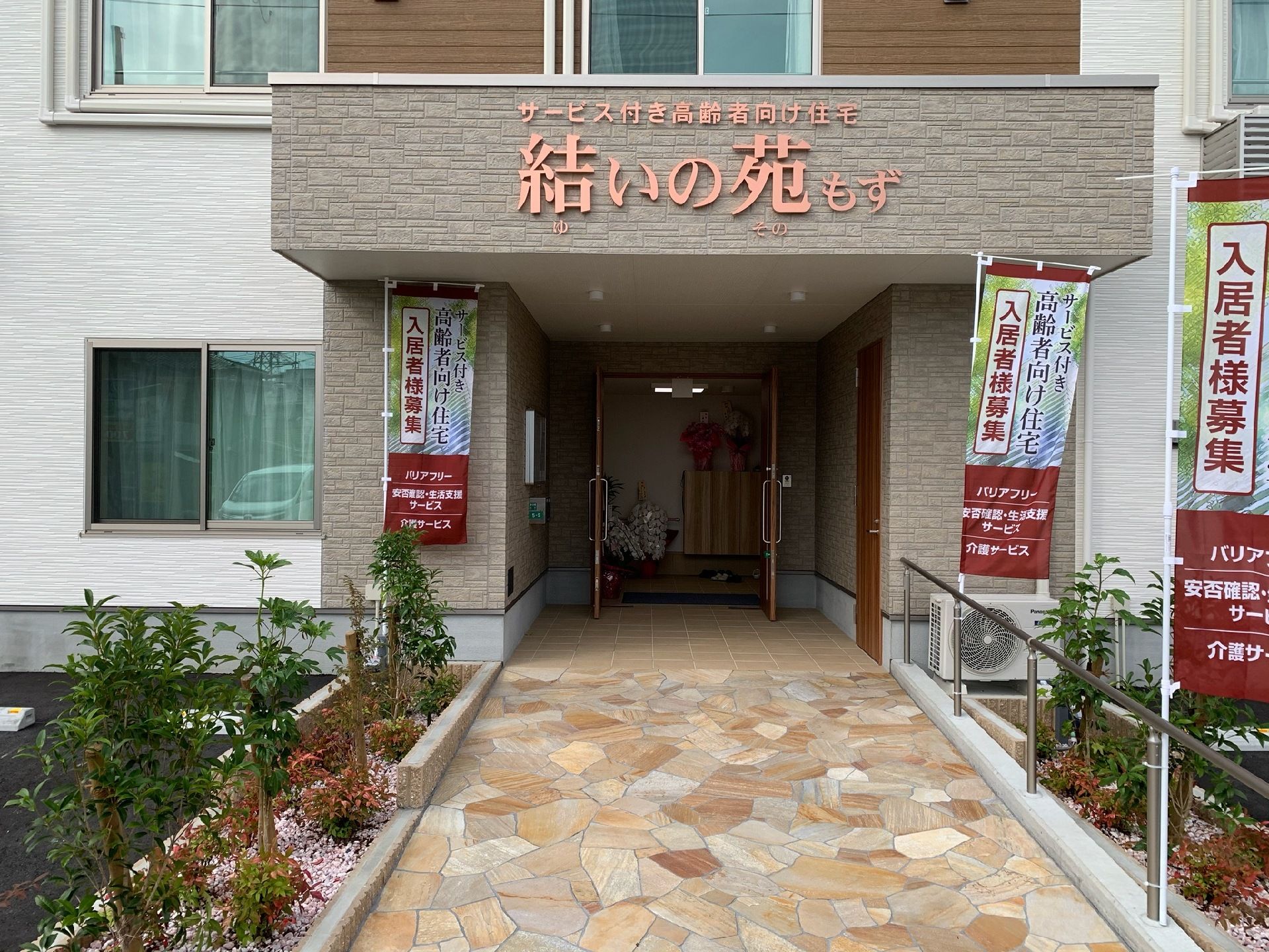 施設の入り口付近、外観を写した写真。結いの苑もずの表示がある雨除けが映っている