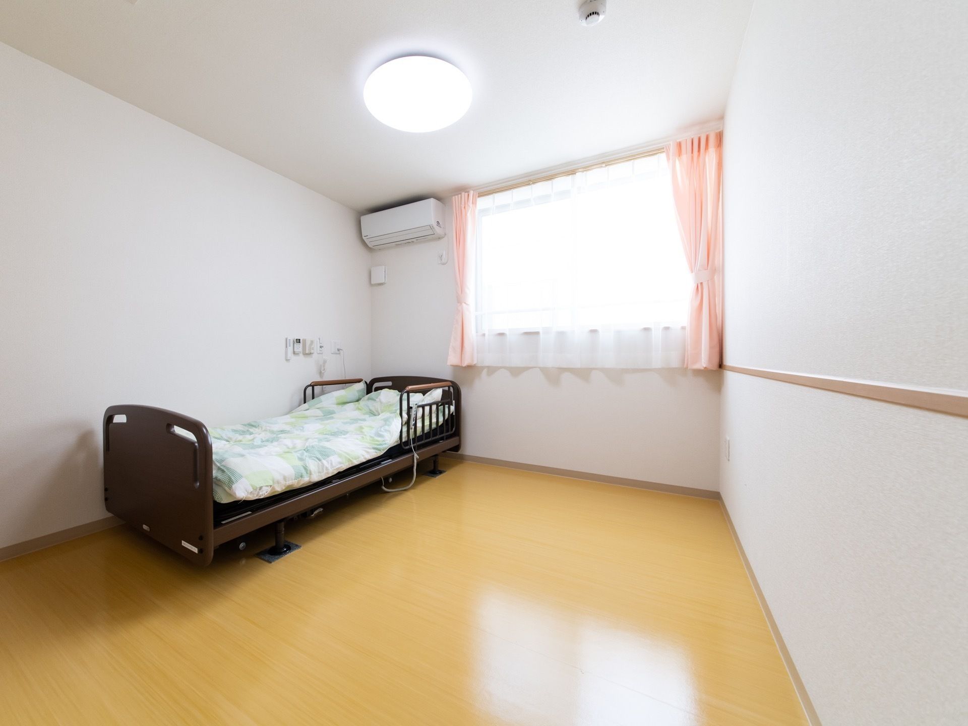 エアコンとベッドが置いてある小さな部屋の様子。窓がついているワンルームタイプの部屋の写真