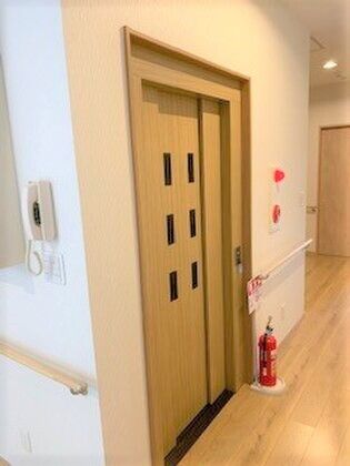 消火器の置かれた廊下にはエレベーターが設置され、すぐそばには手すり付きの階段もある。