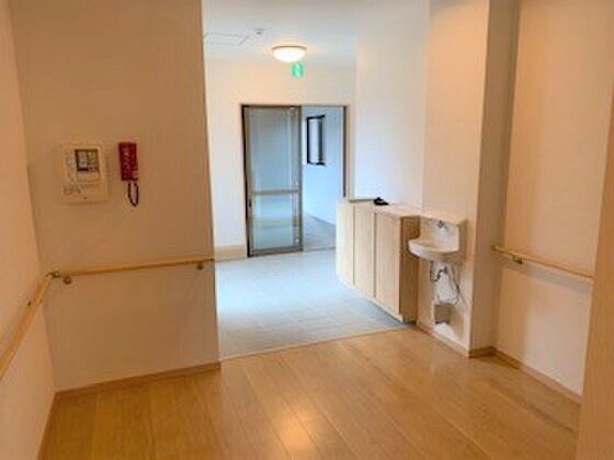 手洗い場が設置されたエントランス葉広く、段差が解消されている。壁には手すりだけでなく緊急用の電話もある。