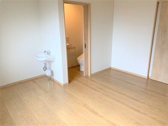 車いす対応の洗面所やスライド式のドアが付いた広いトイレが設置されたフローリングの部屋には家具はない。