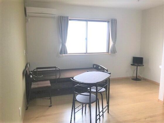 テレビや寝具付きのベッドが置かれたフローリングの部屋にはテーブルセットやエアコンもあり、大きな窓にはカーテンが付いている。