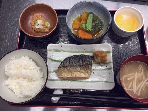 焼き魚と野菜の煮物、納豆ともやしの味噌汁、フルーツのデザートが付いたメニュー