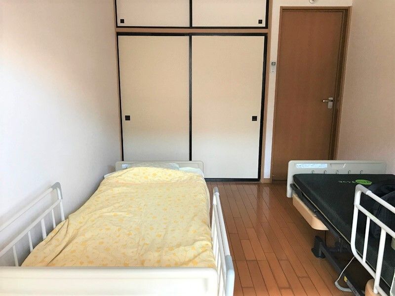 寝具付きのベッドと、何もないベッドが並んで設置されたフローリングの居室。収納スペースも大きい。