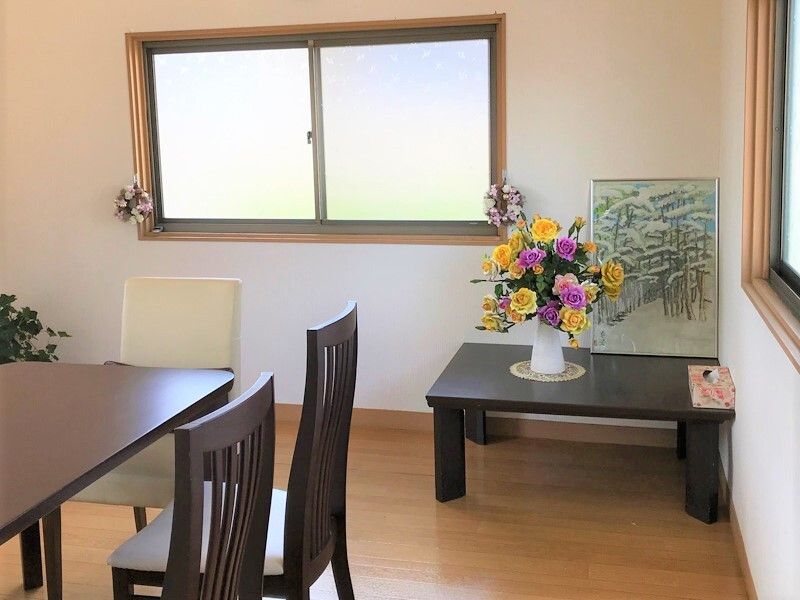 季節の花がきれいに飾られた花瓶がや絵画が置かれたテーブルが窓際にあり、左手にはダイニングテーブルが置かれている。