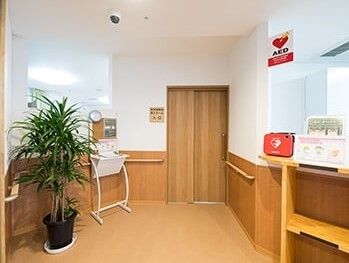 AEDや観葉植物が置かれたエントランス。壁には木目調の手すりが付いている。