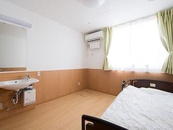 寝具付きのベッドが中央に置かれたフローリングの居室には、エアコンやカーテン付きの窓、洗面所などもある。