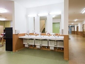 洗面所が３つ並び、それぞれに鏡が付き、奥にはダイニングテーブルが並んだ食堂がある。