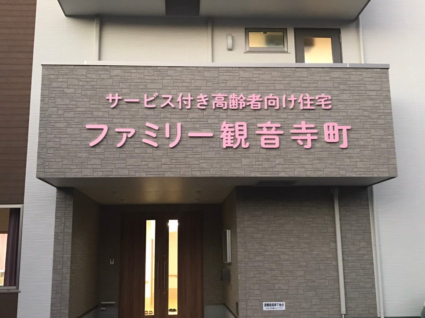 ベッドに寝ている高齢者の女性に話しかけている女性スタッフは花柄エプロンを付けている。