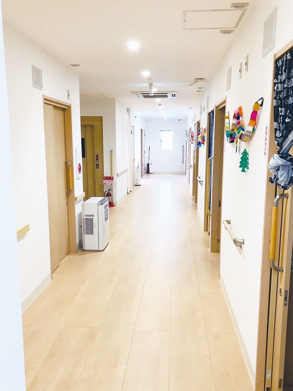 まっすぐな廊下の突き当りの窓から光が入ってきていて、右側には居室のドアが並んでいる。壁には手すりが付き安全に移動できる。
