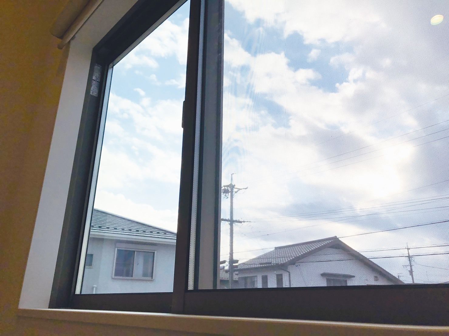大きな窓が付き、窓の外には雲が広がっている空と周りの住宅の屋根の部分が見え、電信柱や電線も確認することができる。