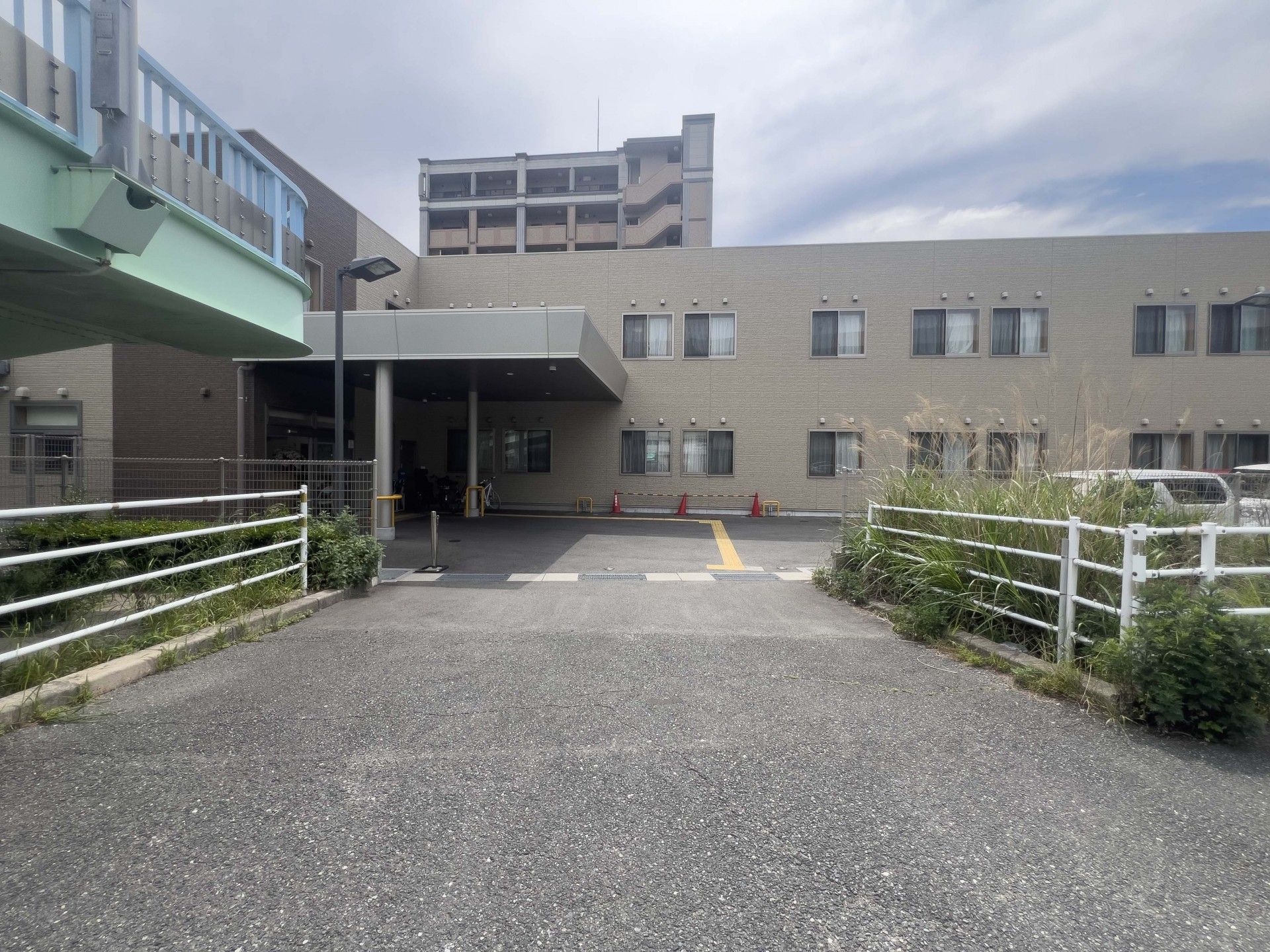 手前にガードレールがあり、ベージュと濃茶の外壁の2階建て有料老人ホーム