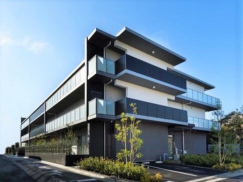 手前に駐車場がある、周囲を植栽で囲んだ三階建ての建物