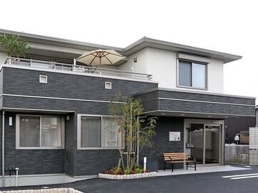 ダークグレーと白の２階建ての建物は玄関に屋根があり、木製のベンチが置かれている。