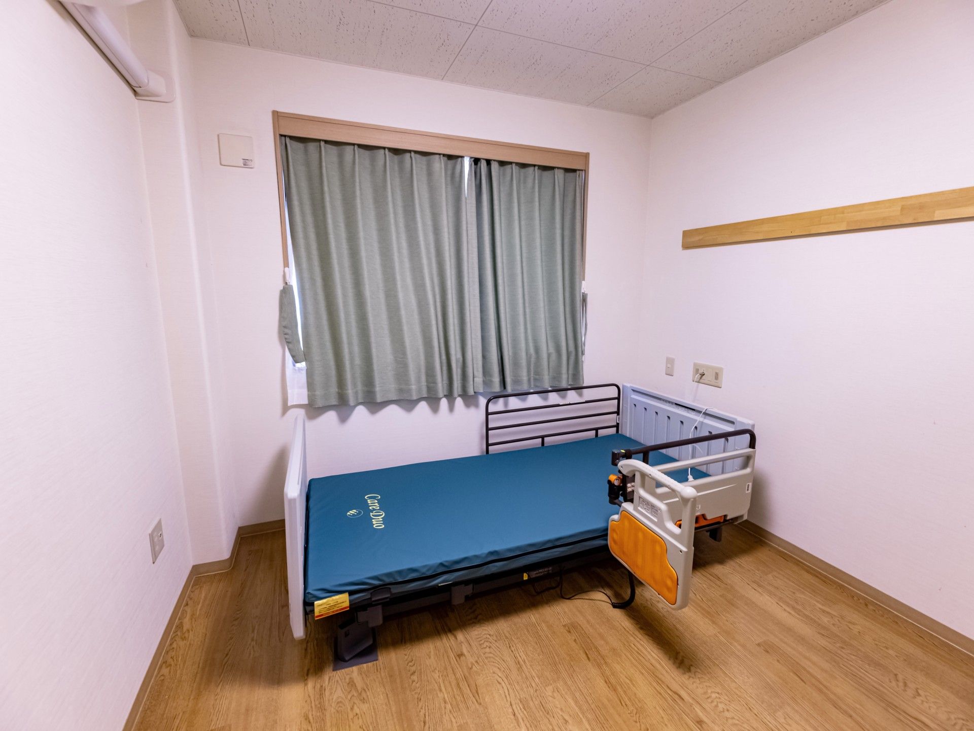 グレーのカーテンと介護用ベッドが完備された部屋