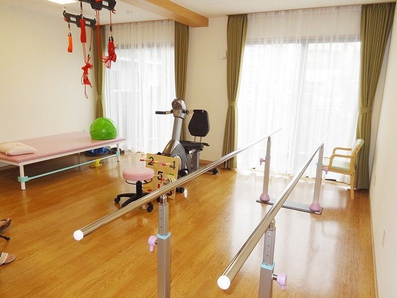 平行棒やベッド、サイクリングマシンなどが置かれたフローリングの共有スペース。天井からはレッドコードがぶら下がっている。