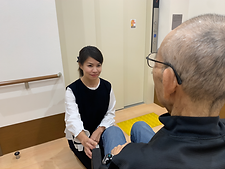 白い花の咲く道を散歩する車椅子に乗った高齢女性と介助をするヘルパー