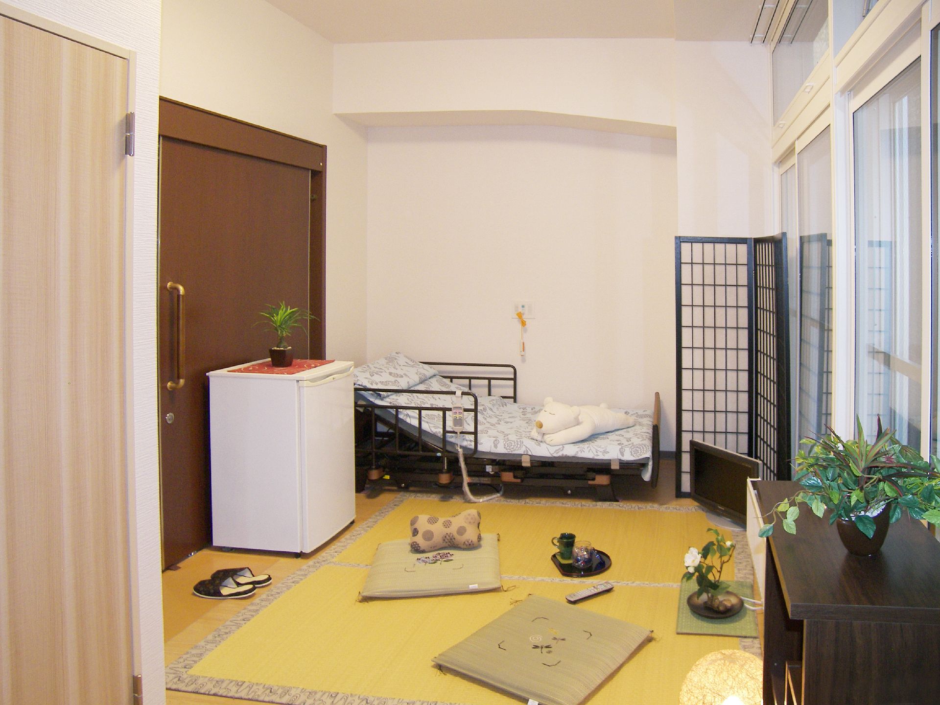 和風のパーテーションが置かれた部屋にはござが敷かれ、座布団が置かれている。寝具付きのベッドのそばには緊急通報装置がある。
