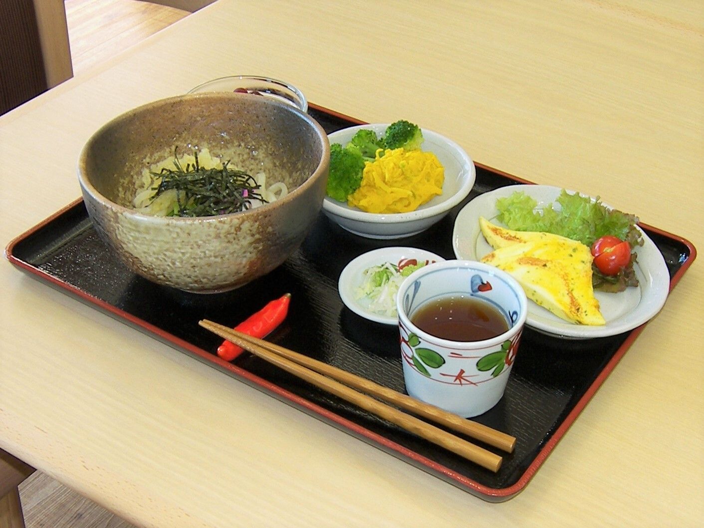 刻みのりが添えられたうどんとオムレツ、お茶、野菜の和え物などがそれぞれ異なる器に盛られている。