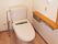 手すりやオレンジの呼び出しボタンが付いたトイレ。操作パネルやトイレットペーパーホルダーも壁に付いている。