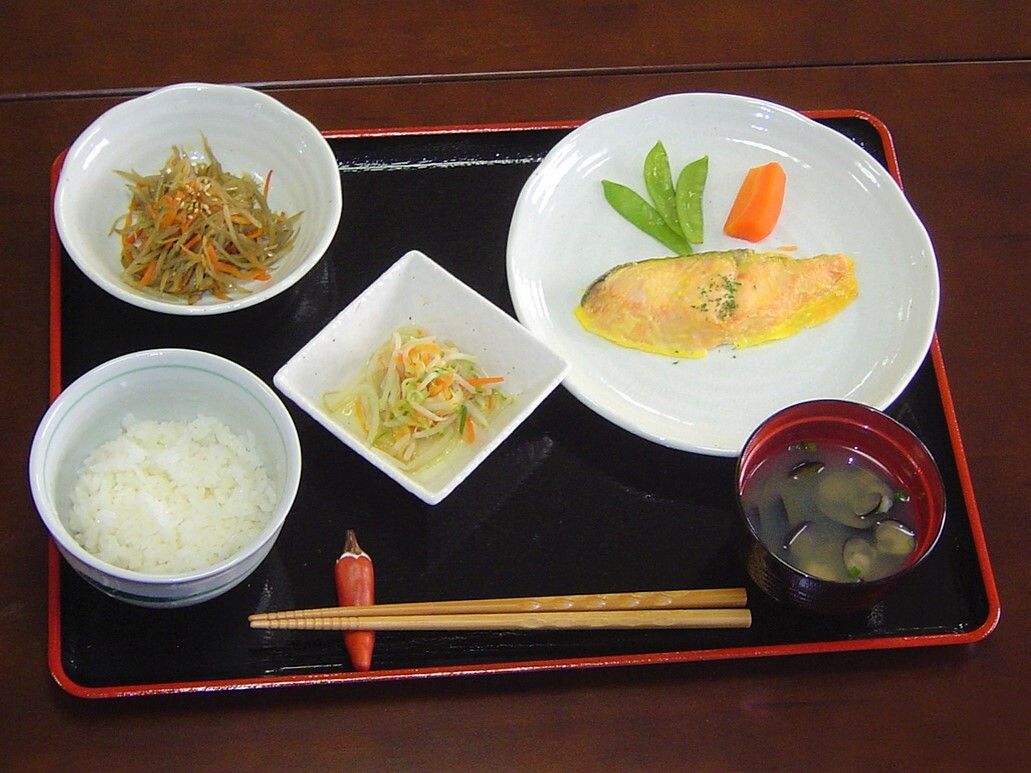 具入りのオムレツや金峰らゴボウ、白いご飯に味噌汁、野菜の和え物などが並んだ黒いトレーには、箸置きと箸もある。