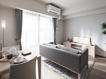 レースカーテンとカーテンが付いた大きな窓があるフローリングの部屋にはエアコンが付き、グレーのソファや寝具がセットされたベッドがある。