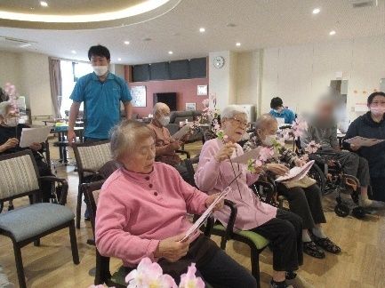 マスクをした男性スタッフが入居者の足をもってマッサージをしている様子。スタッフは階段に座っていて、入居者は車いすに座っている。