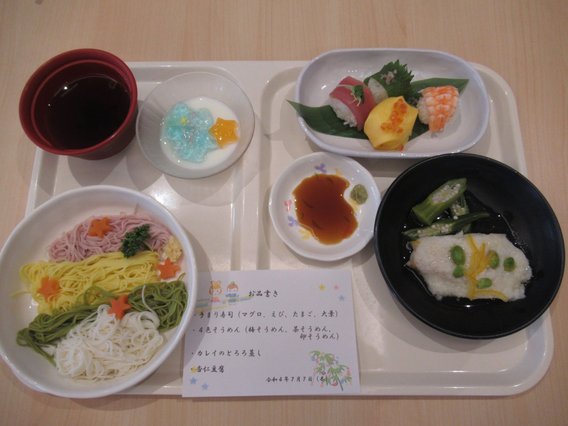 白いご飯に味噌汁、焼き酒や冷ややっこ、ヒジキの煮物、梅干しなどが盛られた器が並んだ木製のテーブル。箸置きには箸が置かれている。