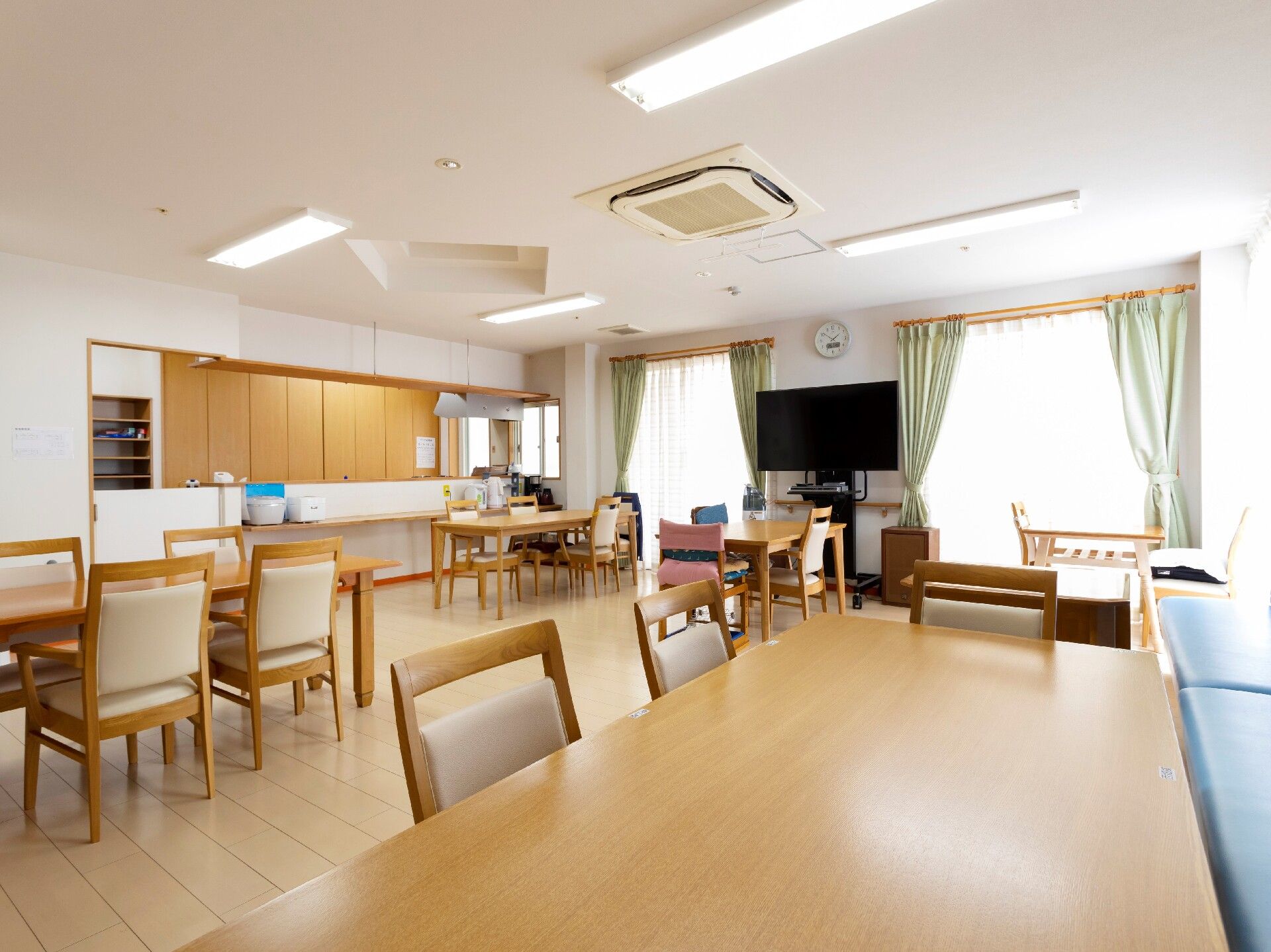 ベージュのソファを囲んで笑顔で話している高齢女性たちの輪の中には白衣を着た女性スタッフがいる。