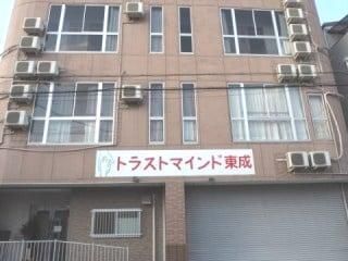 住宅名が書かれているブラウン系の建物は縦に長く、玄関部分には手すりが付いている。