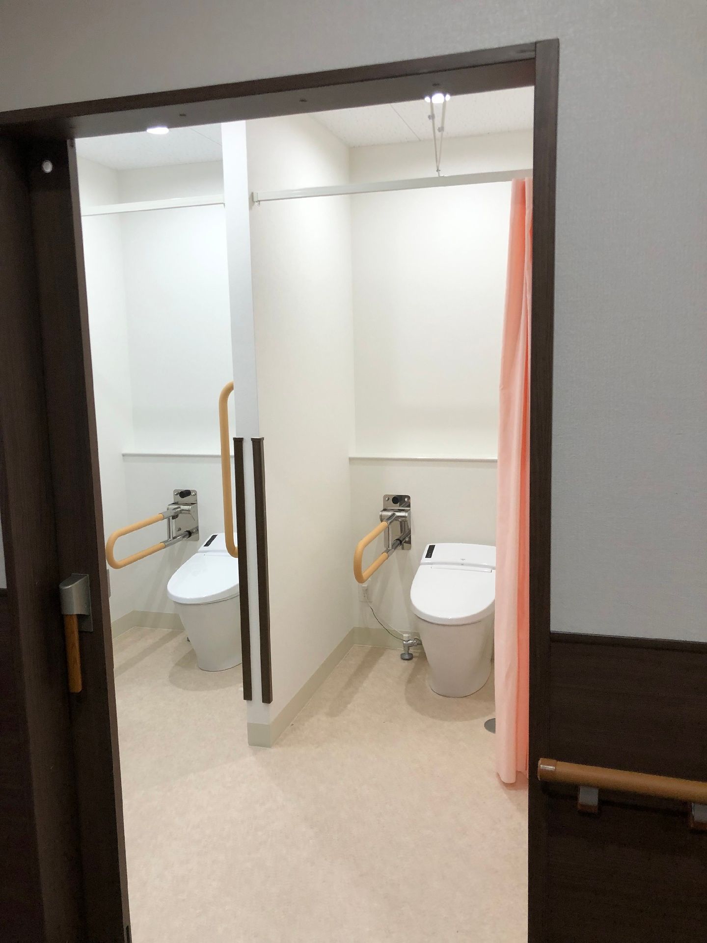 手すりが両サイドに設置されているトイレが二つ並んで設置されている。カーテンで開け閉めするタイプのトイレ。