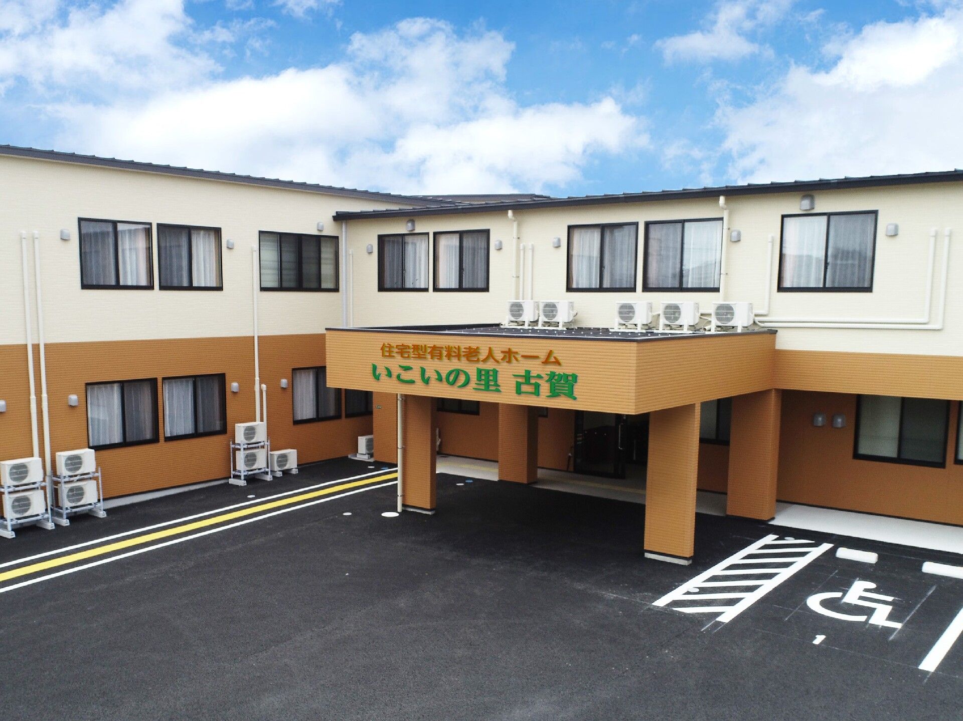 黄色と白の2階建ての建物。玄関部分には車寄せが付き、ベランダや駐車場、駐輪場もある。