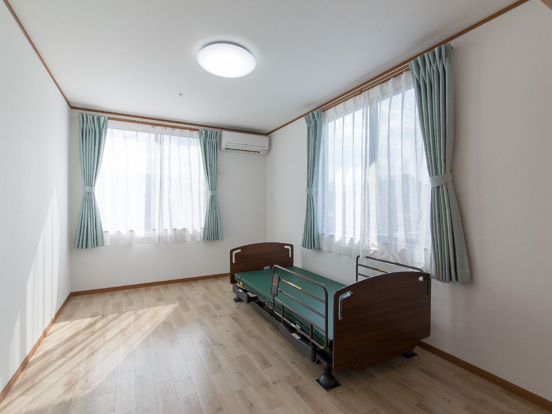 大きな窓が二つ付いたフローリングの部屋には介護ベッドやエアコンがあり、明るい雰囲気。