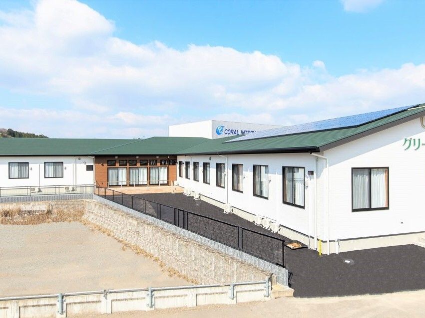 グリーンの屋根が付いた平屋建ての建物の奥には山があり、周りには建物がなく、フェンスが建てられている。