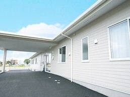 白い外壁の平屋建ての建物。玄関先には大きな車寄せがあり、駐車場も広々としている。