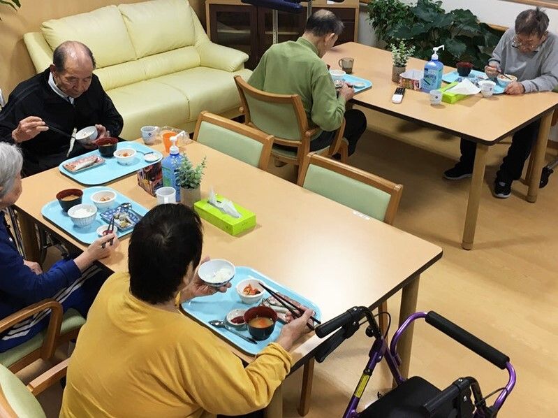 入居者が二つのダイニングテーブルに分かれて食事を楽しんでいる様子。テーブルにはアルコール消毒も置かれている。