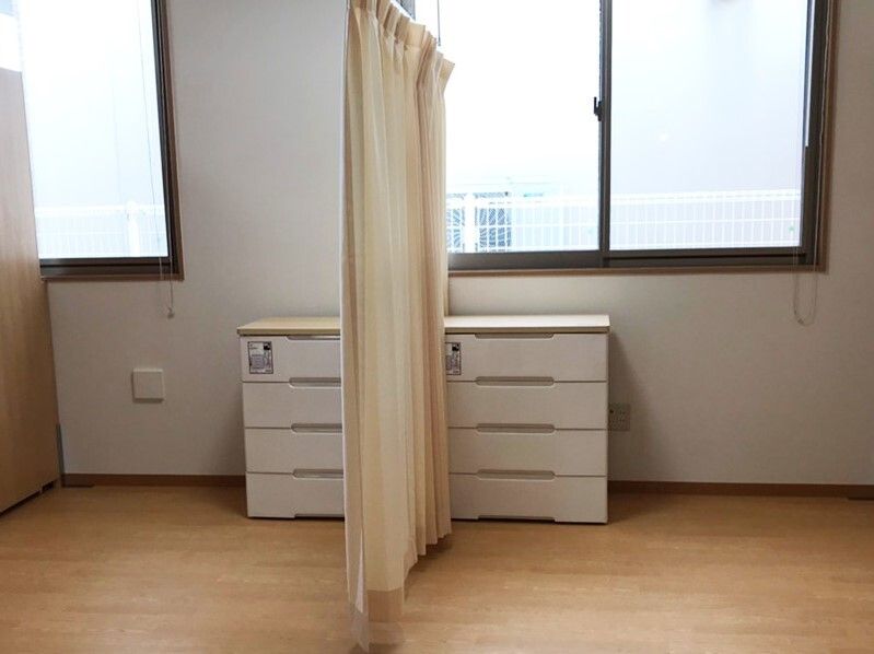 カーテンで仕切られたフローリングの部屋には大きな窓が複数付いている。白いチェストが一人ずつ用意されている。