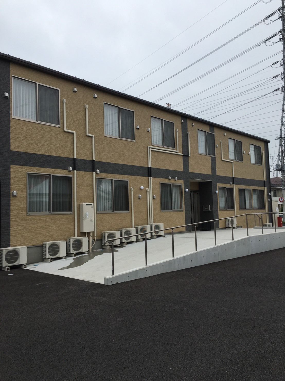 玄関に屋根が付いた2階建ての建物はベージュで、駐車場や屋外階段も完備されている。