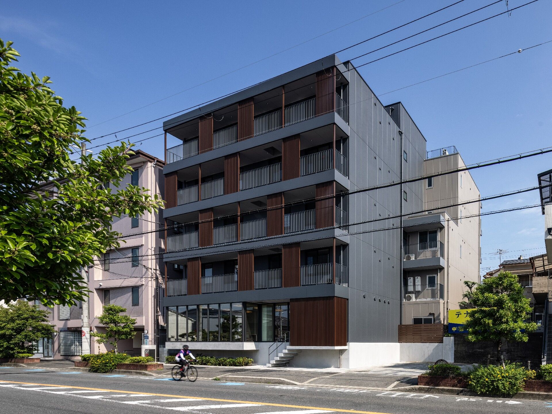 ブラウン系の５階建ての建物はベランダが付き落ち着いた雰囲気。玄関部分には屋根があり、階段も付いている。
