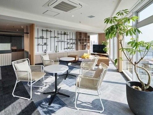 グレーとブルーのカーペットが敷かれたリビングにはテーブルセットが複数置かれ、壁に設置された飾り棚には小物が並び、大きなテレビも置かれている。