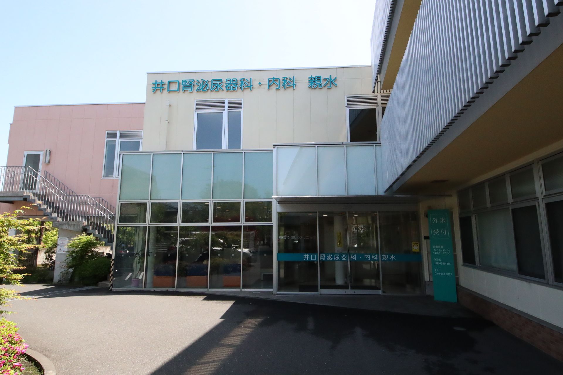 ガラス張りの大きな建物は白を基調としていて、外壁には施設名が書かれ、各フロアにベランダが付いている。建物の上には青空が広がっている。