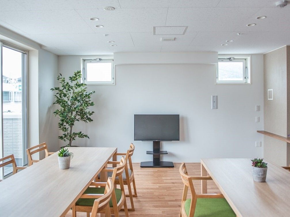 木製のダイニングテーブルが二組置かれ、それぞれのテーブルの上にはグリーンが置かれていて、テレビも設置されている。