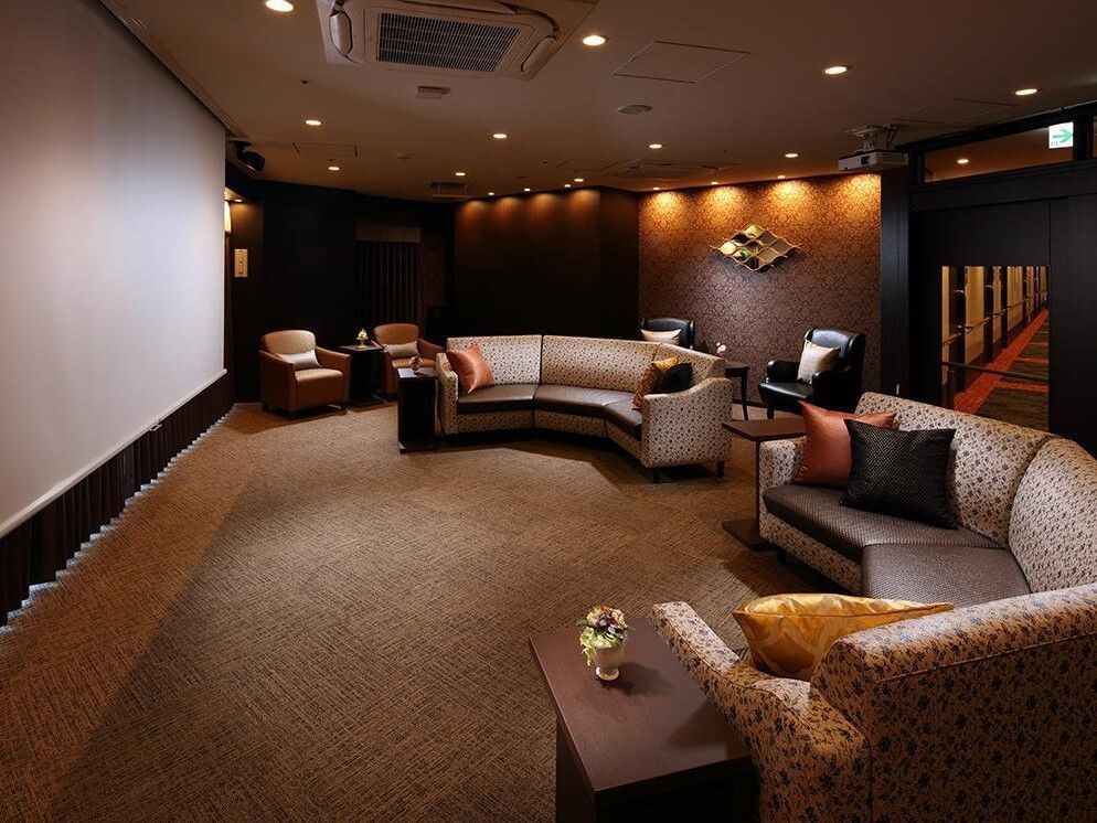 大きなスクリーンと円形に配置されたソファがある、間接照明に照らされた広い部屋