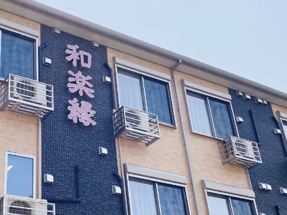 ベージュとダークグレーの外壁の建物を一部アップで撮影した写真。ホーム名がピンクの文字で書かれている。