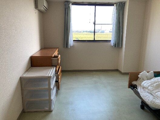 大きな窓が付いている部屋には寝具付きのベッド屋タンス、収納ケースが置かれ、エアコンもついている。