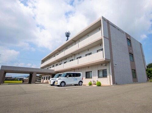3階建ての建物には車寄せやベランダが付き、玄関の周りには木や花も植えられ、駐車スペースもある。