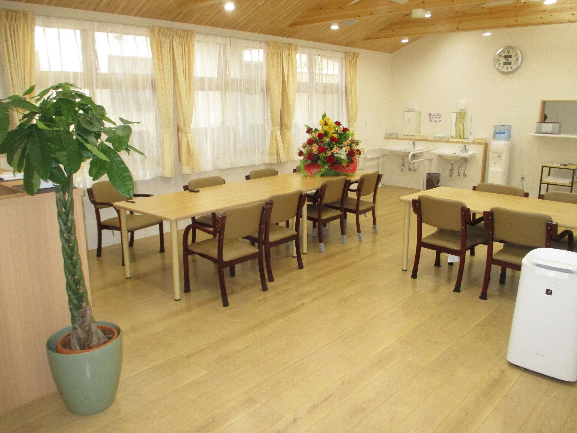 平屋建てのベージュとブラウン、白の建物。玄関には手すり付きのスロープが二つ付き、広い駐車場もある。