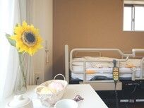 ヒマワリが飾られている居室内には介護ベッドが置かれ、窓にはカーペットが付いている。